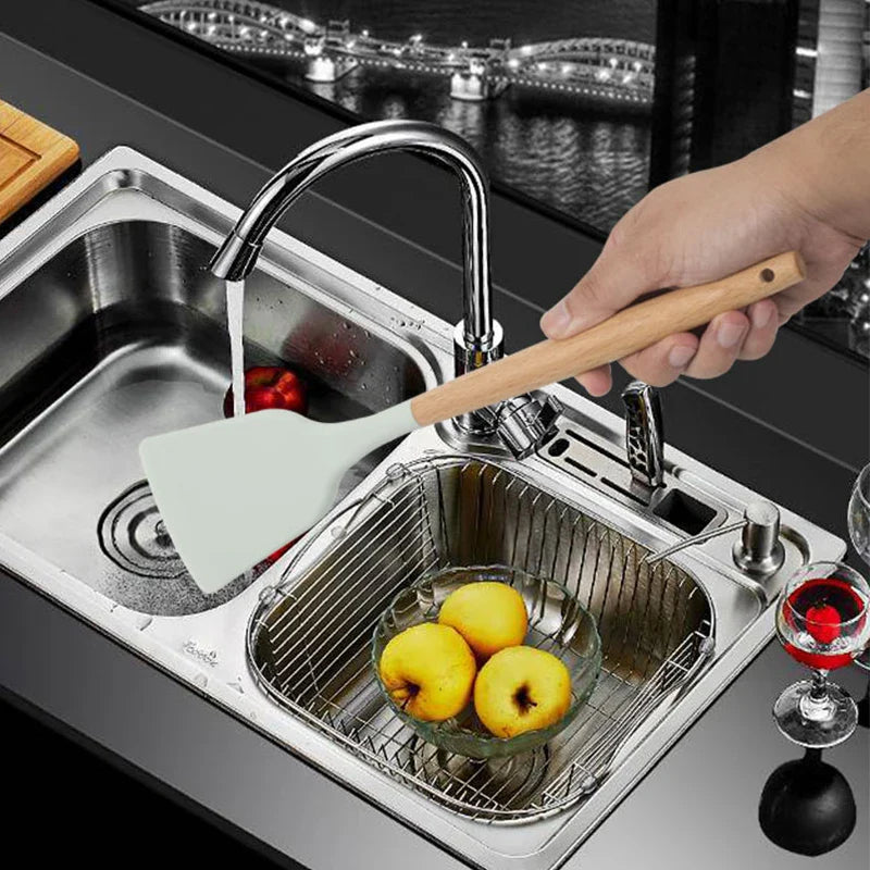 Silicone spatula with wooden handle washing fruits in kitchen sink.